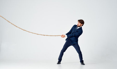 business man in a suit pulls a rope on a light backgroundの写真素材