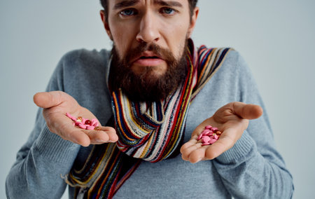 man with pills in his hands scarf around his neck health problems cold dissatisfactionの写真素材
