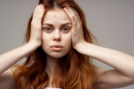 woman with loose hair touches her head with hands white t-shirt gray backgroundの写真素材