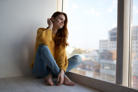 pretty woman sits on the windowsill and looks out the window rest charm interior