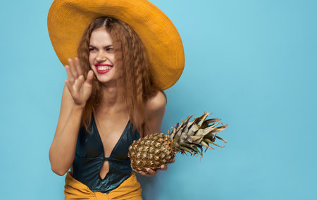 Smiling woman in hat exotic fruits pineapple tropics blue backgroundの写真素材