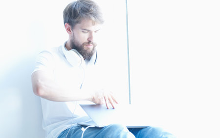 man with laptop sitting on windowsill keyboard monitor headphones model