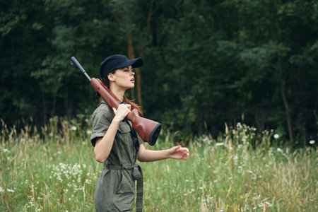 Woman on nature the gun on the shoulder green jumpsuit black cap green leavesの写真素材