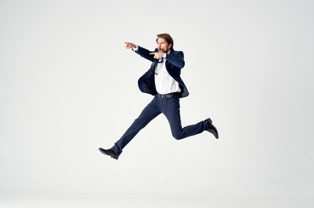 Energetic business man in a blue suit jumps up on a light background success joy emotionsの写真素材