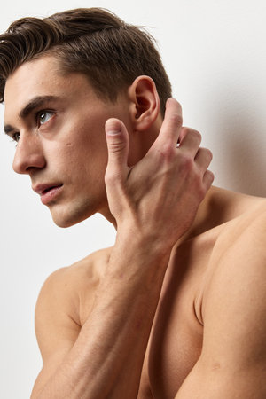 A sexy guy with a naked torso touches his face with his hand and looks to the sideの写真素材