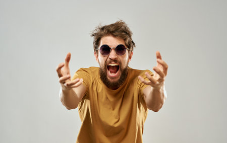 Emotional man in yellow t-shirt glasses gesturing with hands gray backgroundの写真素材
