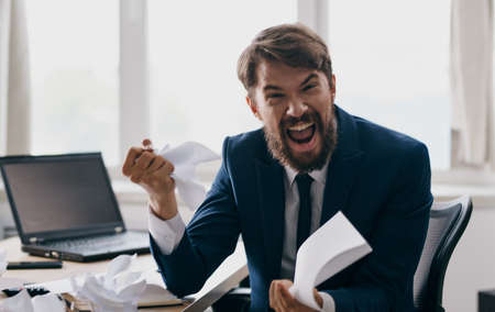 Aggressive man with sheets of paper in hands stress irritability business laptop financeの写真素材