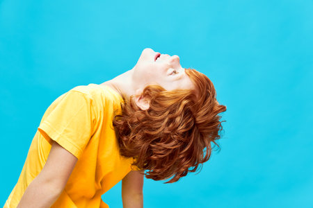 Red-haired boy with his head thrown back looks up blue backgroundの写真素材