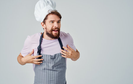 A cook in a headdress is gesturing with his hands on a light background, success emotionsの写真素材