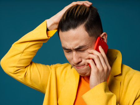 Asian man talking on the phone and touching his head with his hand on a blue backgroundの写真素材