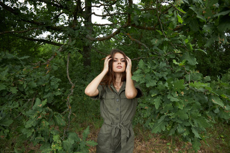 Woman outdoors Green jumpsuit straightens her hair against the backdrop of the forest fresh air natureの写真素材