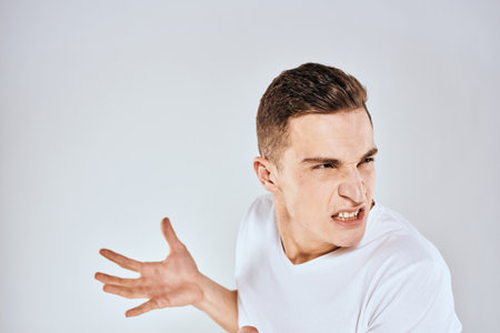 Emotional man gestures with his hands displeasure white t-shirt light backgroundの写真素材