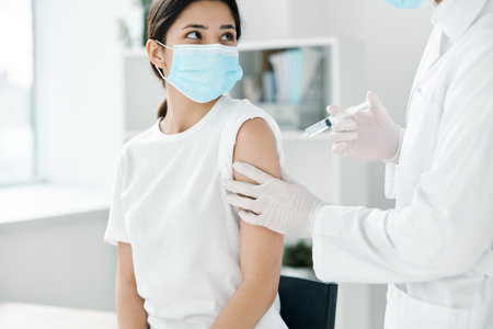 doctor in protective gloves holds a womans hand and injects a vaccine against covid-19 coronavirusの写真素材