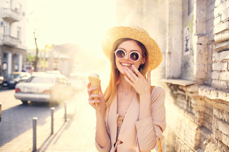 Pretty woman in sunglasses and a hat on the street walk with ice creamの写真素材