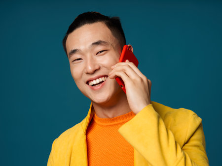 Happy Asian man talking on the phone and laughing on a blue backgroundの写真素材