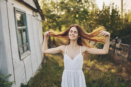 happy woman in a white sundress near the building in nature and trees in the backgroundの写真素材