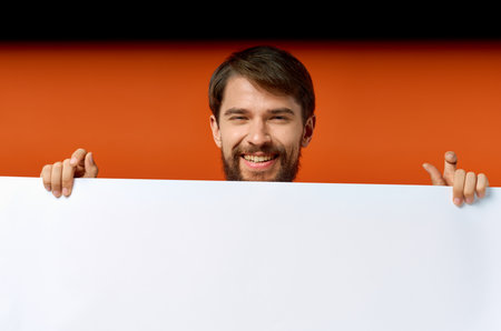 ad poster in the hands of a man on an orange background gesturing with his hands Copy Space mockupの写真素材