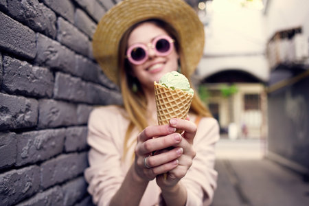 Woman in sunglasses and a hat with ice cream walking through the city brick wall outdoorsの写真素材