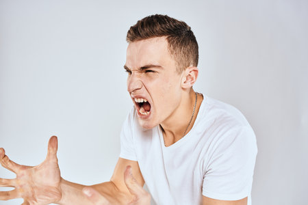 Emotional man gestures with his hands displeasure white t-shirt light backgroundの写真素材