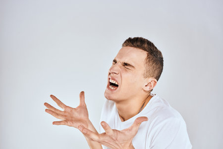 Emotional man gestures with his hands displeasure white t-shirt light backgroundの写真素材