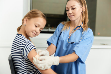 a woman doctor in a dressing gown seals a childs hand with a plasterの写真素材