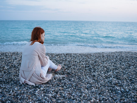 woman on a rocky beach in a sweater and pants and the ocean in the backgrounの写真素材