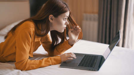woman lying on bed with laptop working at home communication technology