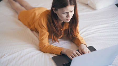 woman lies in bed in front of laptop typing work at home