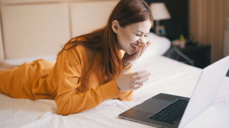 cheerful woman in the bedroom lies on the bed in front of the laptop communication