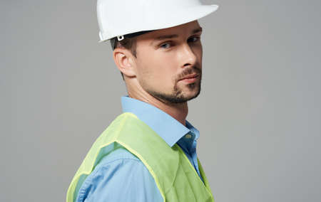 A male worker in a yellow vest and a white helmet on a gray background