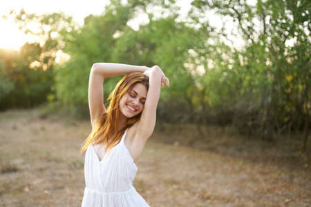 romantic woman in a dress gestures with her hands outdoors near green treesの写真素材