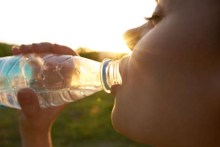 happy woman with bottle of water in nature sun trees green grass summerの写真素材