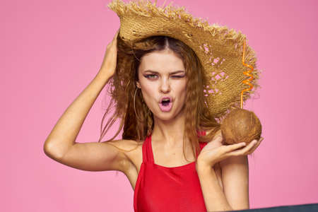Woman with coconut cocktail in straw hat exotic vacation summer pink backgroundの写真素材