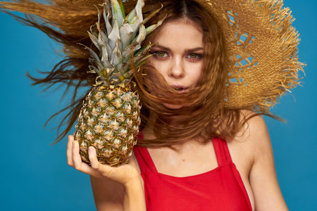 Woman in a straw hat with pineapple in her hands wavy hair exotic fruits you summer blue background vacationの写真素材