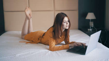 woman in bedroom lies in bed in front of laptop message restの写真素材