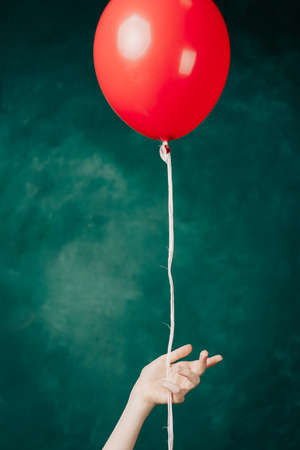 red balloon in hand on a green background flies up close-upの写真素材