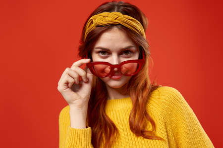 pretty woman in yellow sweater red glasses fashionable clothes close-up red backgroundの写真素材