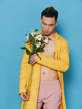 Portrait of a man of Asian appearance on a blue background with a bouquet of white flowers and a yellow coatの写真素材