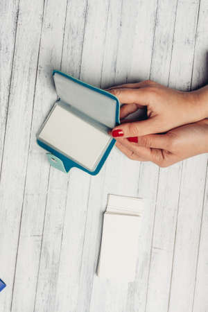 blue card holder in female hands and white sheet of paper wooden background textureの写真素材