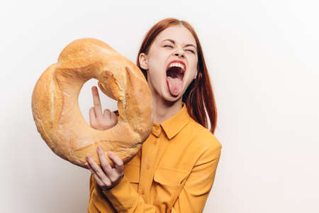woman in a yellow shirt holds a round loaf on a light background and emotions modelの写真素材