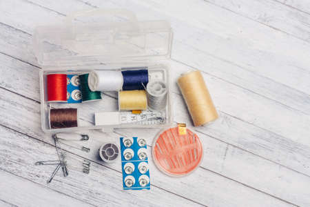skein of multicolored thread in a plastic box wooden background needles safety pin sewing supplies