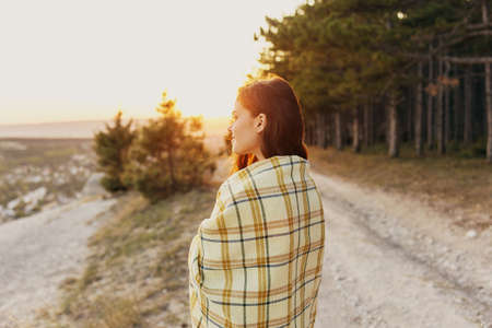 A woman on the road near the forest looks to the side and a plaid on her shouldersの写真素材