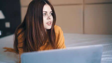 cheerful woman lies in bed in front of laptop internet vacation