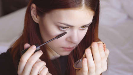 woman paints eyelashes with a mirror in hand self-care femininityの写真素材