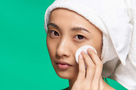 pretty asian woman bare shoulders towel on head cotton pad clean skin green backgroundの写真素材