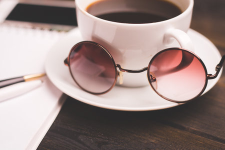 cup of coffee on a saucer wooden table notepad pen office stationeryの写真素材