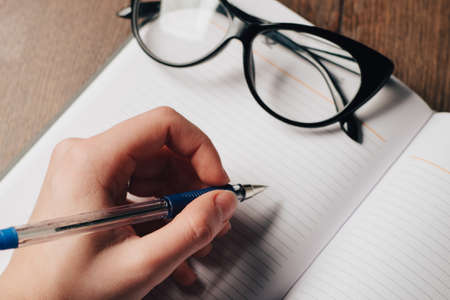 notepad writing glasses on the table pen in handの写真素材