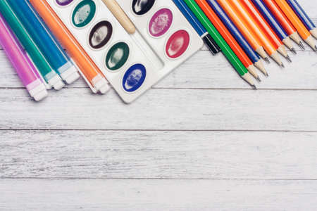 colored pencils watercolor paints and markers pens on wooden table school education