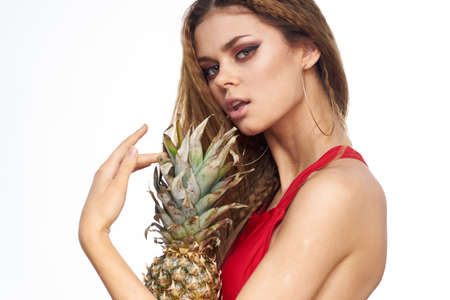 Woman with pineapple in hands wavy hair red t-shirt fruits summer vacation light background