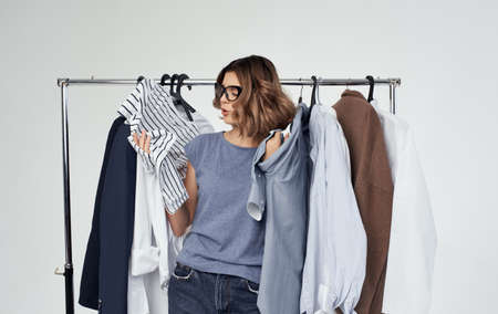 Emotional woman stands near clothes on a hanger in a dressing room on a light shopping backgroundの写真素材
